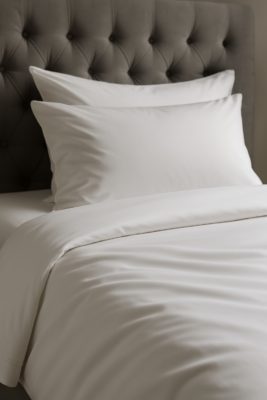 Strak opgemaakt bed met wit Egyptisch katoen dekbedovertrek en kussens, luxe uitstraling in hotelkamerstijl
