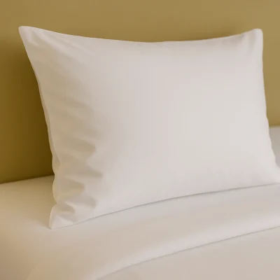 Strak opgemaakt hotelbed met een wit kussen in een gladde kussensloop tegen een beige hoofdbord.