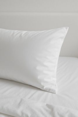 Strak hotelbed met witte kussensloop; subtiele glans en gladde textuur tonen het verschil tussen katoen, satijn en percale voor ademend slaapcomfort.